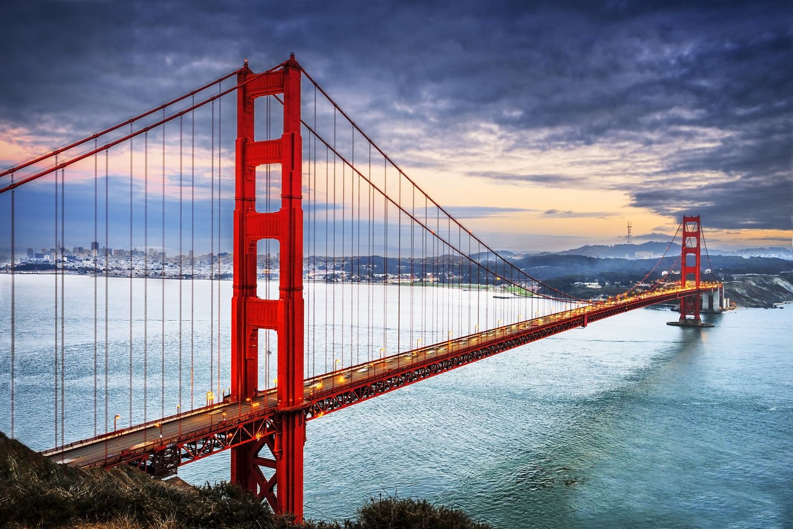 The red Golden Gate Bridge at dusk with the San Francisco skyline behind it